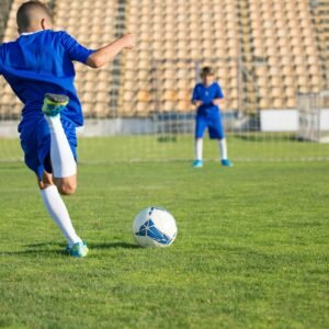 Two boys in blue uniforms practice soccer on a sunny field, focusing on the ball.
